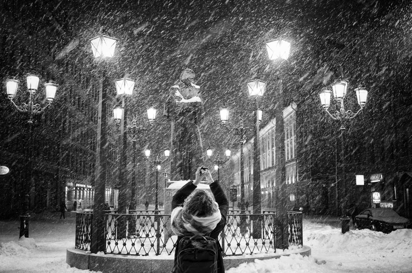 Woman photographing a statue at night in a snow storm